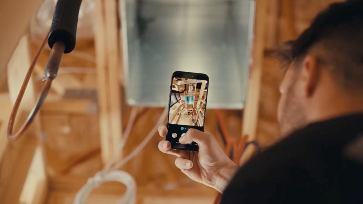 Person taking photos of a framed wall cavity with exposed plumbing and structural components.