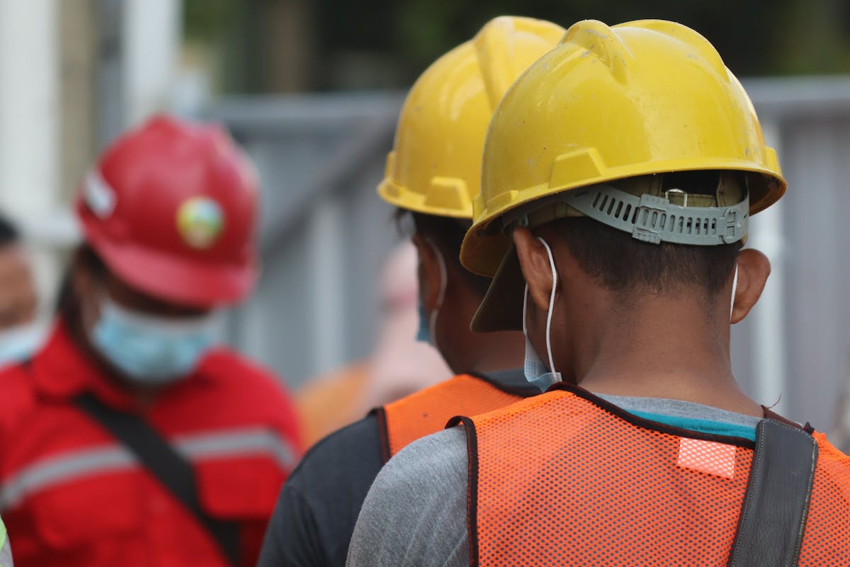 Construction crew wearing hard hats and safety vests gather for onsite job briefing.