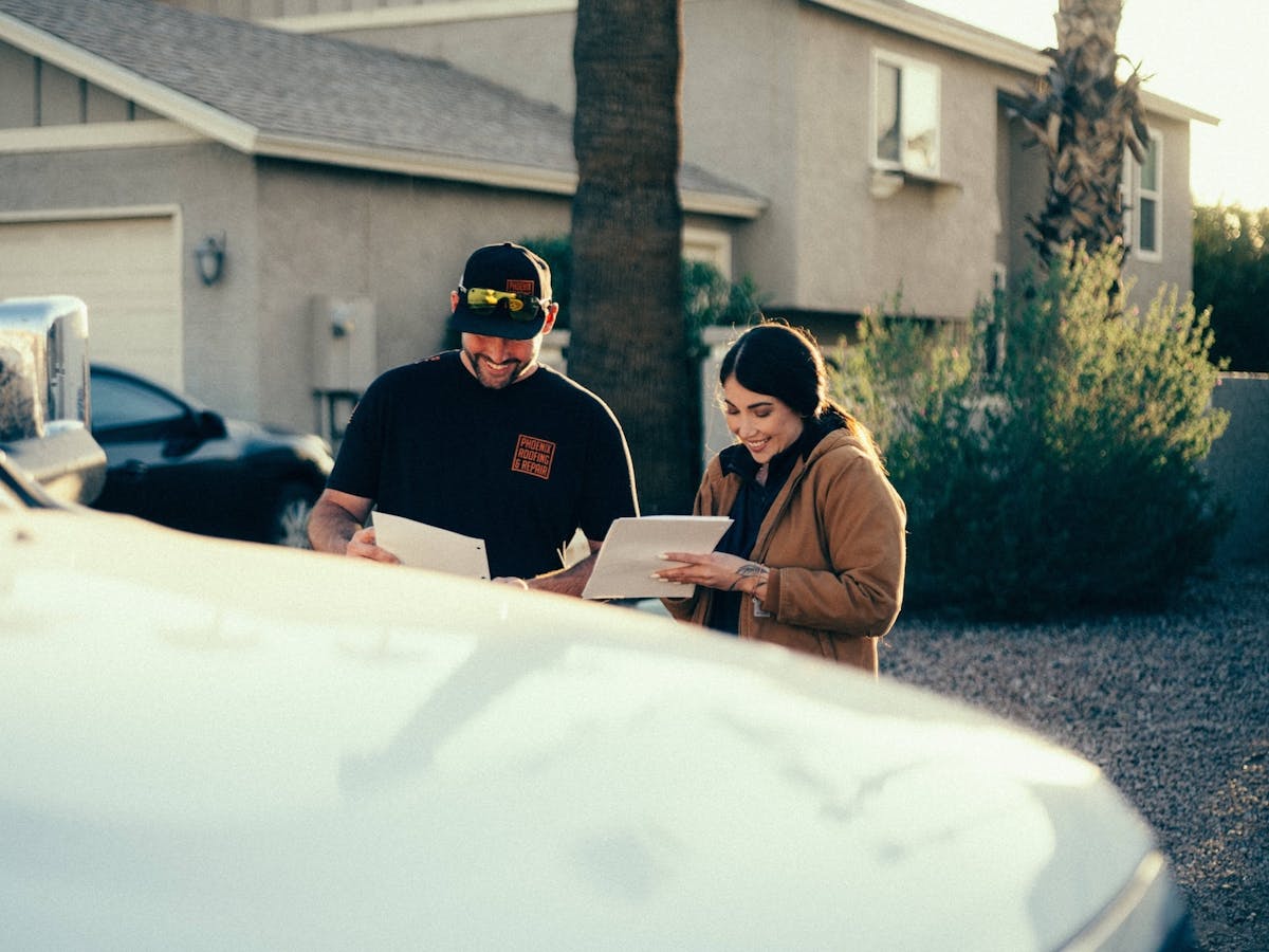 two people standing outside a home and reviewing paperwork together