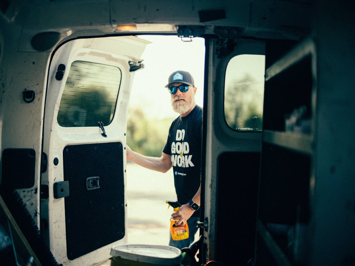 Worker stands at open van door holding supplies while preparing for tasks on job site.