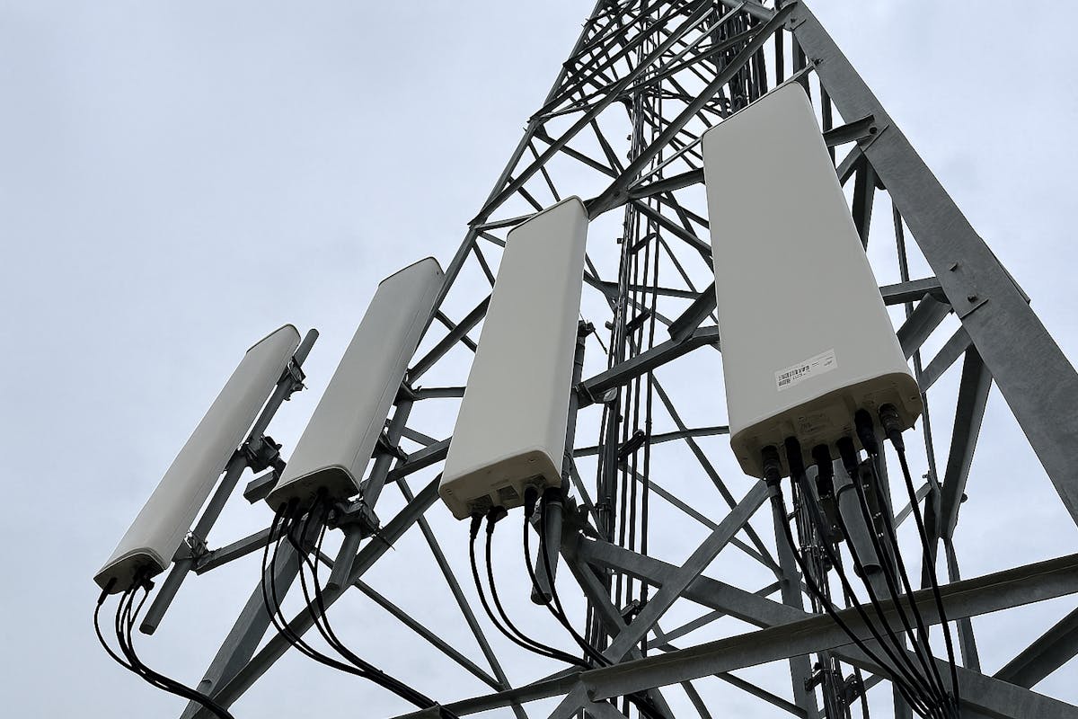 Upward angle photo of a steel lattice cell tower with multiple newly installed panel antennas and secured cable runs, captured from ground level